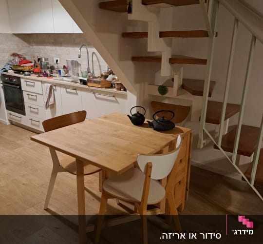 חלל מגורים מסודר הכולל שולחן אוכל מעץ, מדרגות ומטבח